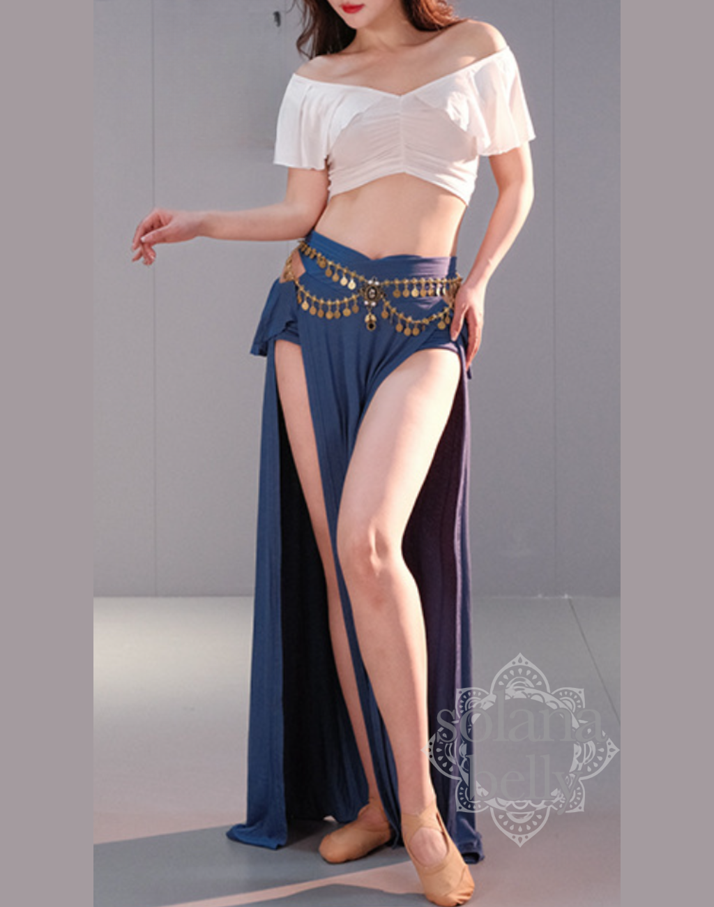 ベリーダンス レッスン着 衣装のホワイト×ブルーのセットアップを着用した女性。肩まわりを美しく見せる白トップスと、脚長効果のあるブルースカートの組み合わせ。初心者向けの安心デザイン。