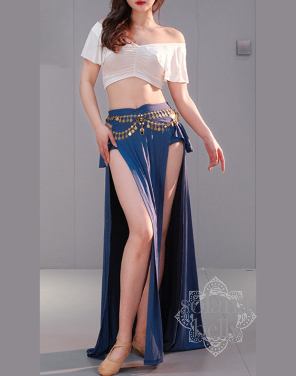 ベリーダンス レッスン着 衣装のホワイト×ブルーのセットアップを着用した女性。肩まわりを美しく見せる白トップスと、脚長効果のあるブルースカートの組み合わせ。初心者向けの安心デザイン。