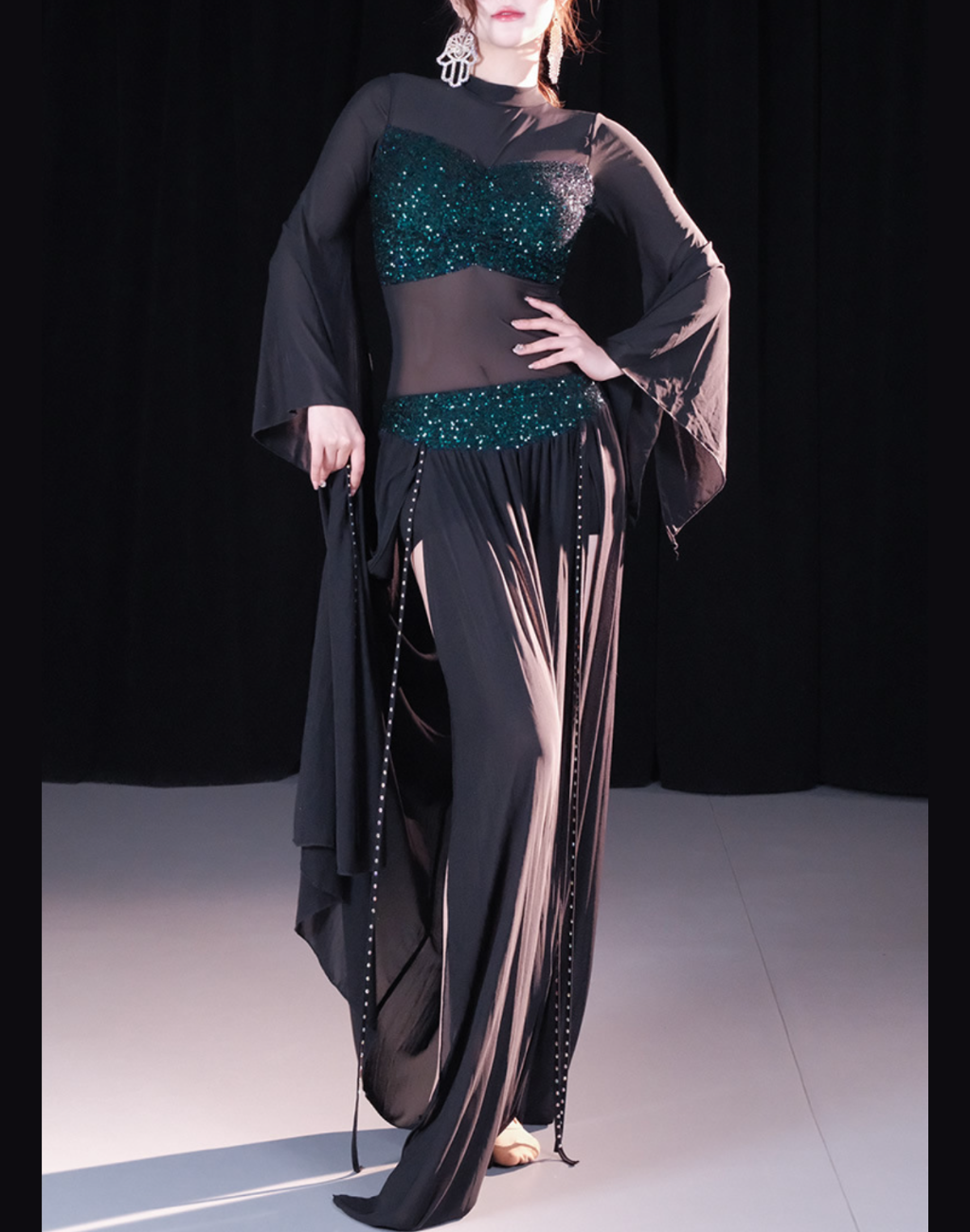 黒のトップスとスカートが一体となったデザインを着用するベリーダンス レッスン着 衣装、袖口が広がりワンピース風に見えるスタイル