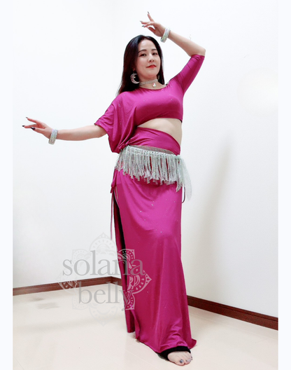 ピンクのベリーダンス レッスン着を着た女性が腕を広げて立つ姿。衣装の滑らかなドレープが上品に流れ、レッスン中の動きを美しく見せる。