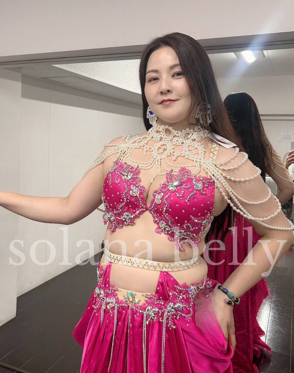 ピンクのベリーダンス衣装に、小粒パールのドレープネックレスを合わせた発表会控室での着用画像