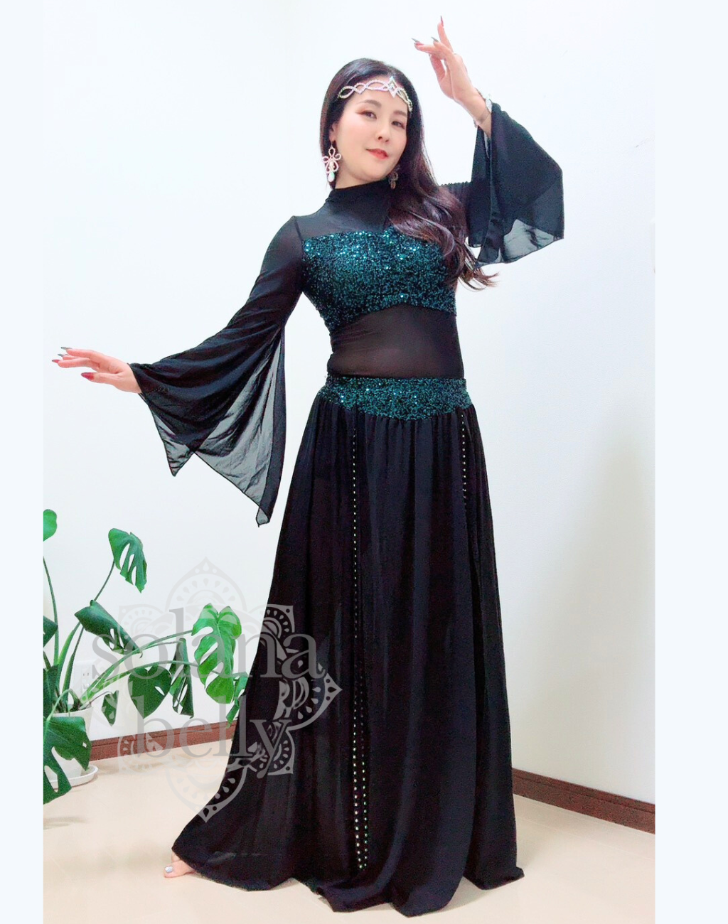 黒のトップスとスカートが一体となったデザインを着用するベリーダンス レッスン着 衣装、袖口が広がりガラベーヤワンピース風に見えるスタイル