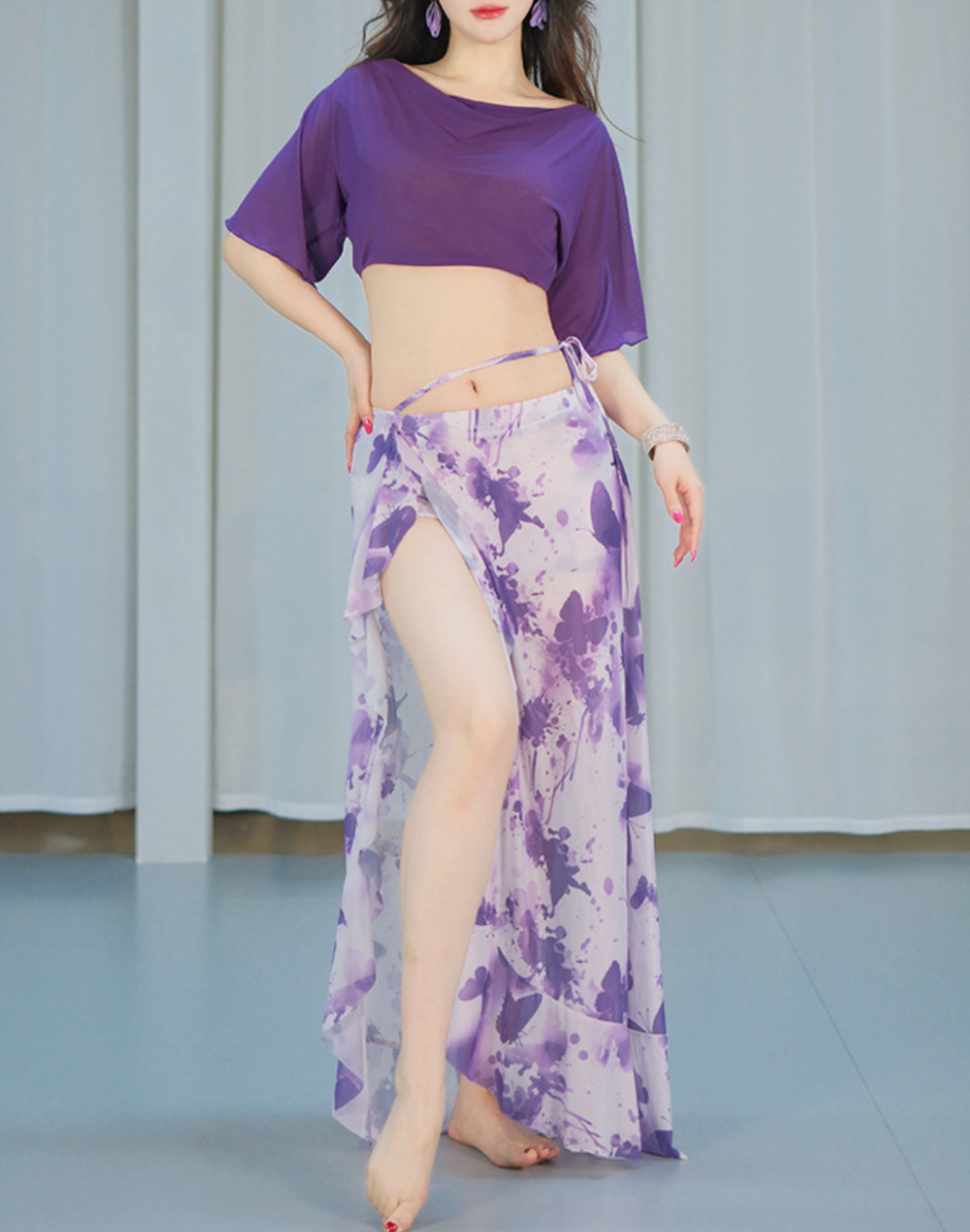 紫のバタフライ柄のセットアップを着た女性がポーズを取る姿。ベリーダンスのレッスン着としても衣装としても映える落ち着いたデザイン。