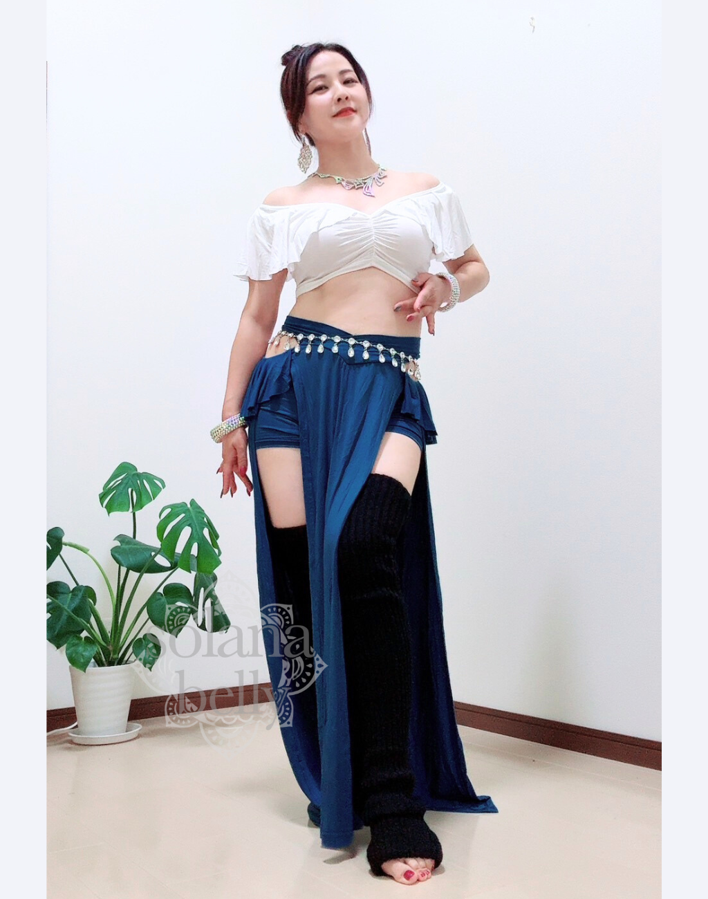 ベリーダンス レッスン着 衣装のホワイト×ブルーのセットアップを着用した女性。肩まわりを美しく見せる白トップスと、脚長効果のあるブルースカートの組み合わせ。初心者向けの安心デザイン。