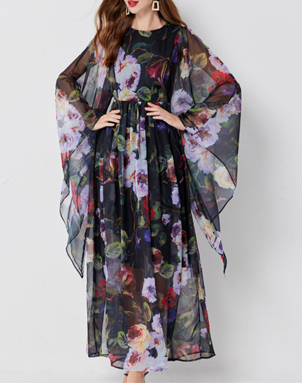 黒地に大ぶりの花柄が描かれたガラベーヤワンピースを正面から着用して立つ女性。
ベリーダンス衣装やレッスン着の上に羽織れるデザインで、ゆったり広がる袖が柔らかく揺れている様子。