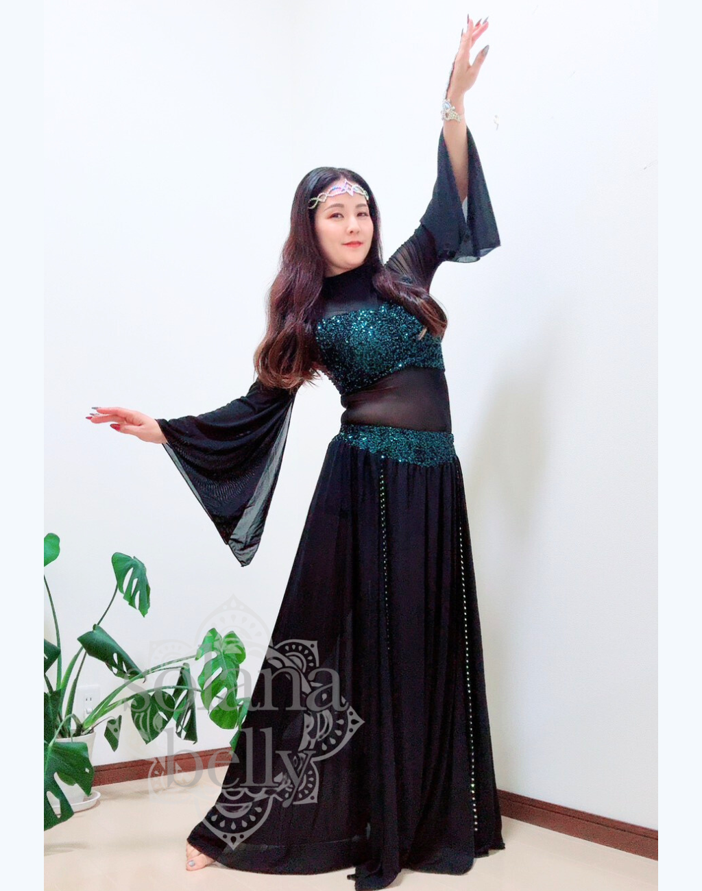 黒のトップスとスカートが一体となったデザインを着用するベリーダンス レッスン着 衣装、袖口が広がりガラベーヤワンピース風に見えるスタイル