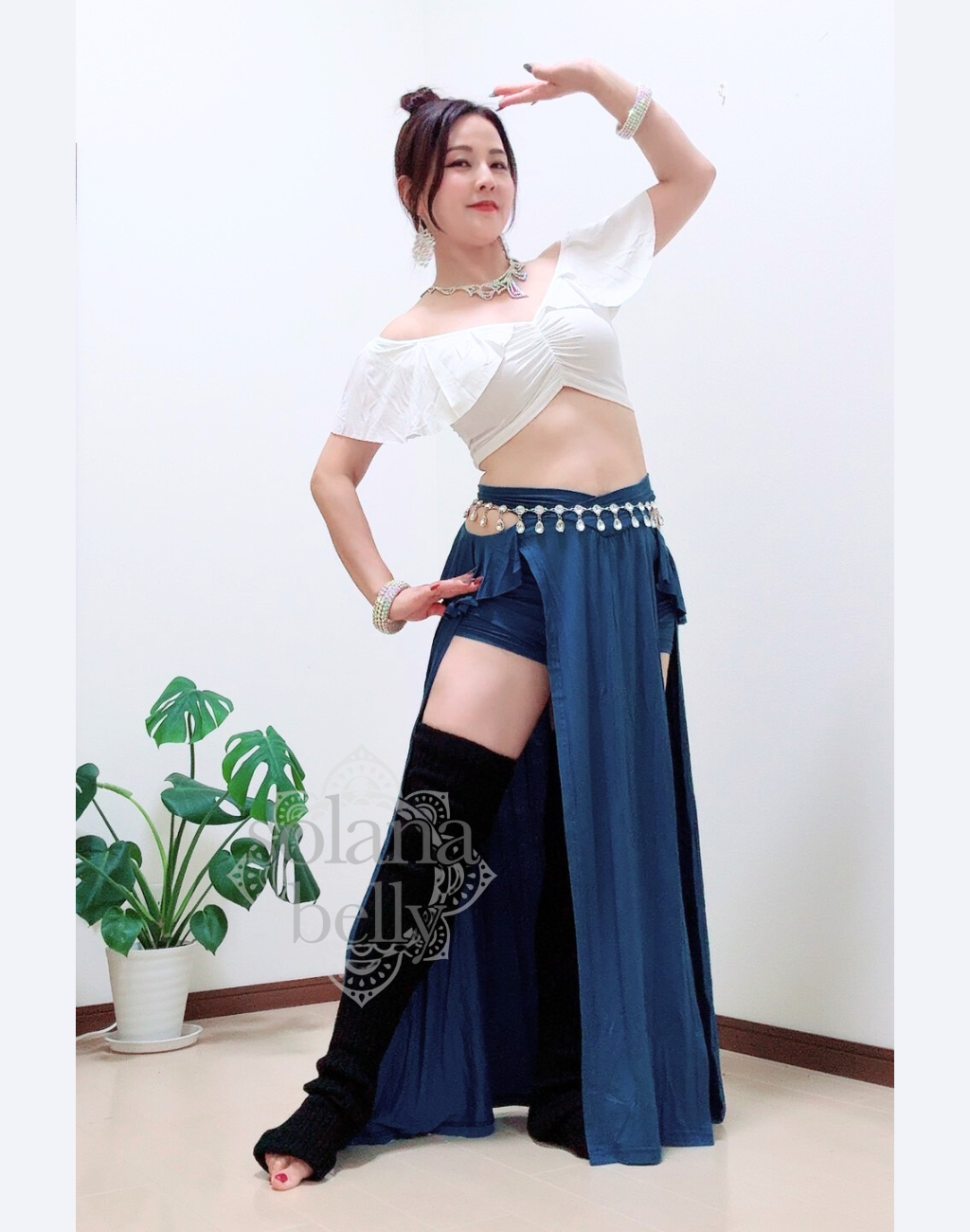 ベリーダンス レッスン着 衣装のホワイト×ブルーのセットアップを着用した女性。肩まわりを美しく見せる白トップスと、脚長効果のあるブルースカートの組み合わせ。初心者向けの安心デザイン。