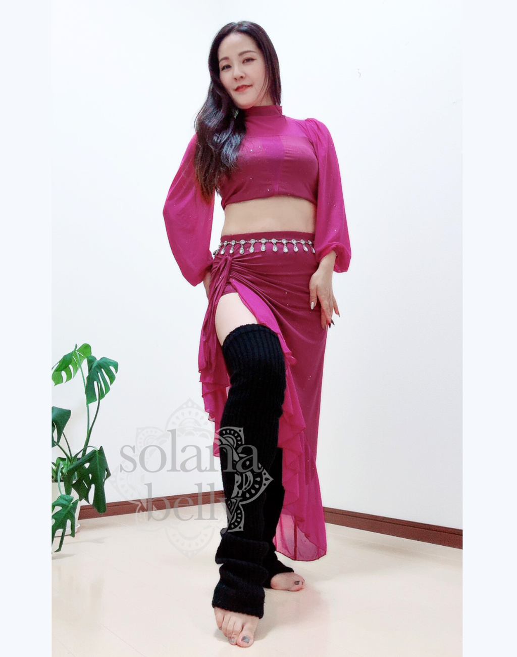 正面を向いた全身ショット。ピンクのセットアップを着た女性が立ち姿でポーズを取り、透け感のある袖が腕の動きを柔らかく見せている。ベリーダンスの基礎練習に最適なレッスン着で、衣装に着替える前の準備にも使いやすい。