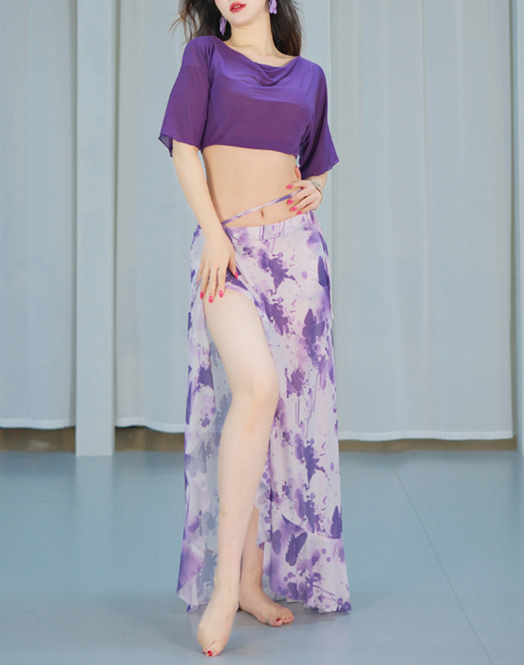 パープルのレッスン着を着た女性が腕を広げて舞う瞬間。袖の揺れが美しく、ベリーダンス衣装としても印象に残るデザイン。