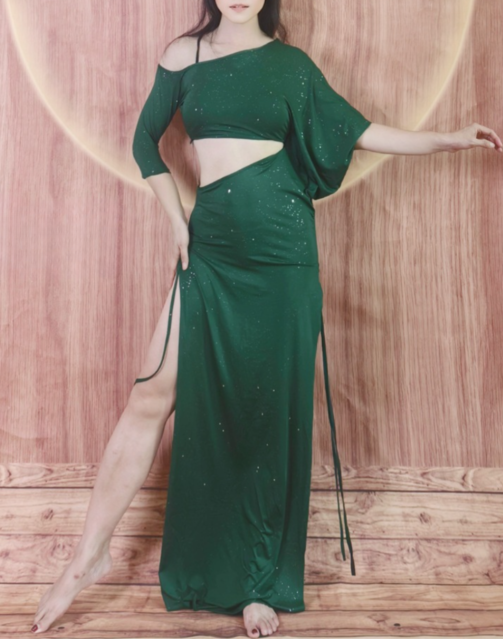 深みのあるグリーンのベリーダンス レッスン着を着た女性が、片足を前に出して立つ姿。衣装のドレープが美しく流れるワンピースタイプ。