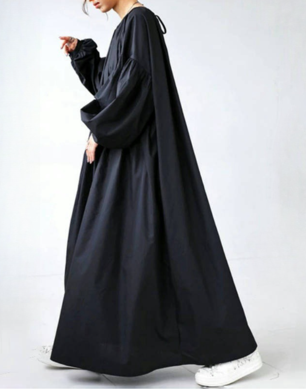 黒のガラベーヤワンピースを着たモデルが横向きで歩く姿を撮影。ハリのある生地が足元まできれいに広がり、ベリーダンスの衣装やレッスン着の上からも軽く羽織れるゆったりとしたシルエットが分かる構図。