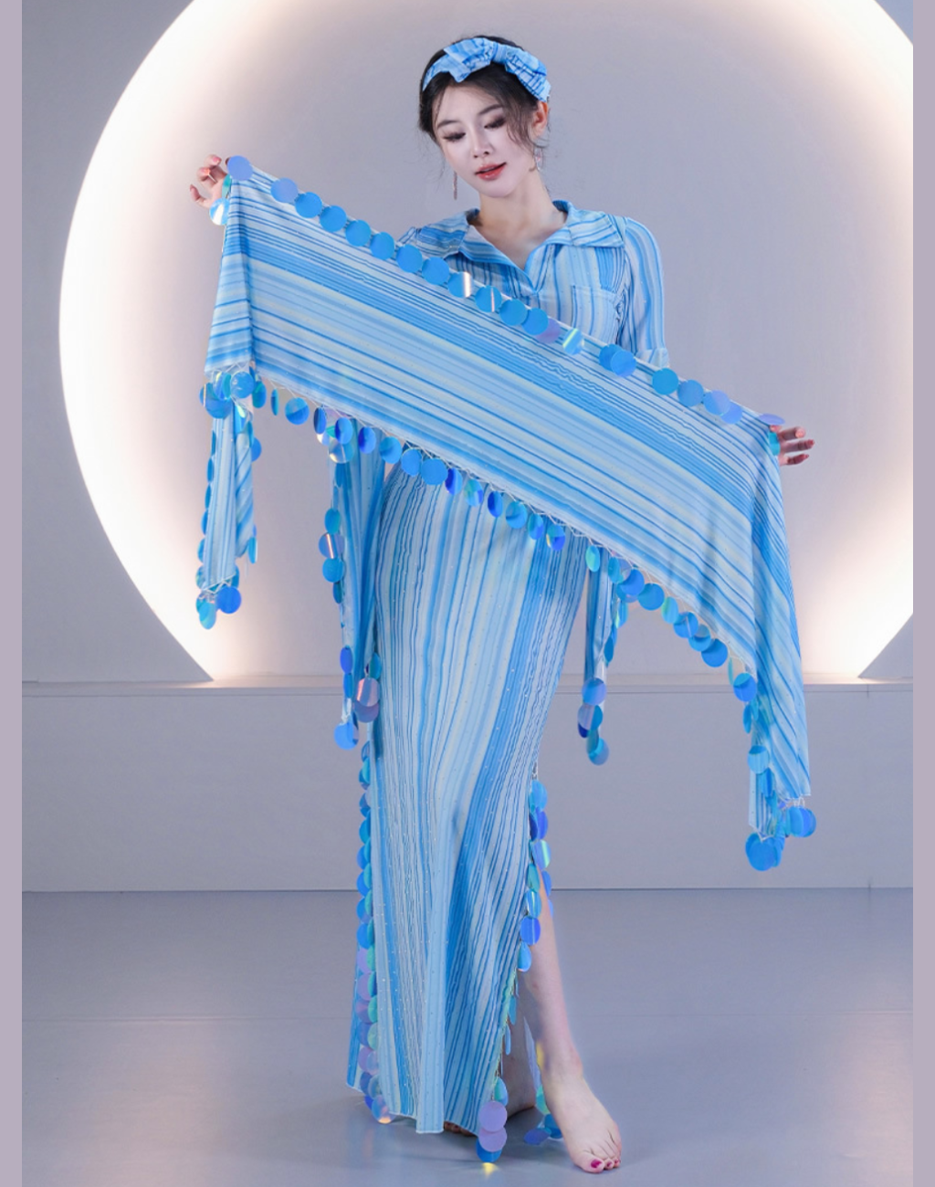 ブルーのバラディドレスのストライプ生地を両手で広げた着用画像。光を反射する丸型スパンコールと細かな縦縞模様が特徴のベリーダンス衣装。