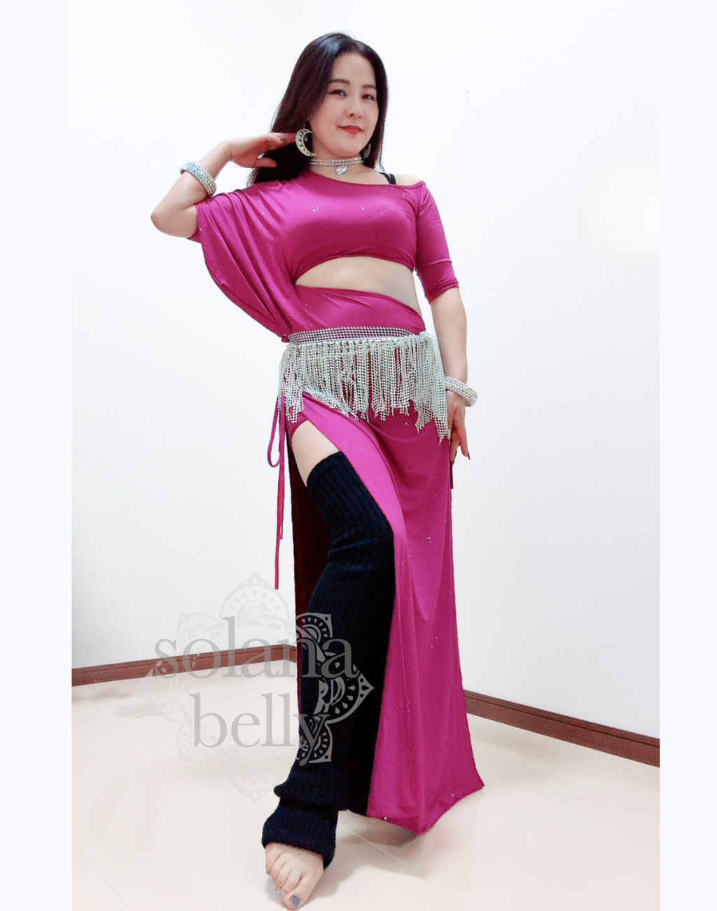 ピンクのベリーダンス レッスン着を着た女性が腕を広げて立つ姿。衣装の滑らかなドレープが上品に流れ、レッスン中の動きを美しく見せる。