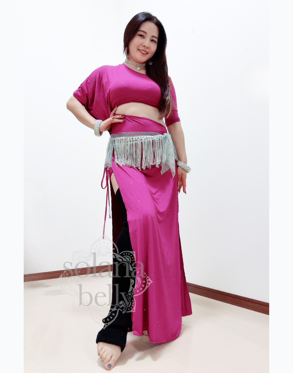 ピンクのベリーダンス レッスン着を着た女性が腕を広げて立つ姿。衣装の滑らかなドレープが上品に流れ、レッスン中の動きを美しく見せる。