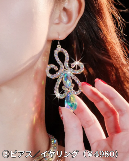 ベリーダンス衣装に合わせるアクセサリーとして、オーロラビジューのピアス／イヤリングが耳元で揺れ、指先に光が反射している動きのある構図の画像。